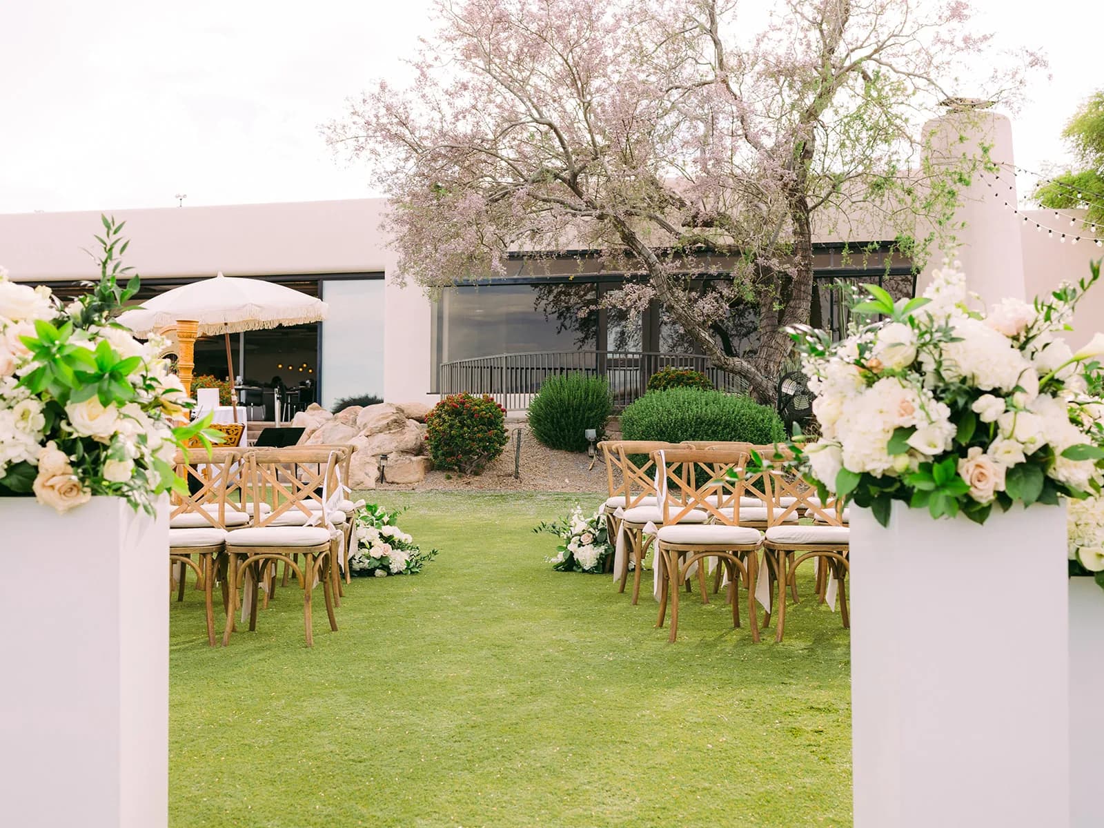 Lawn ceremony with white floral arrangements and cross-back chairs at Adero